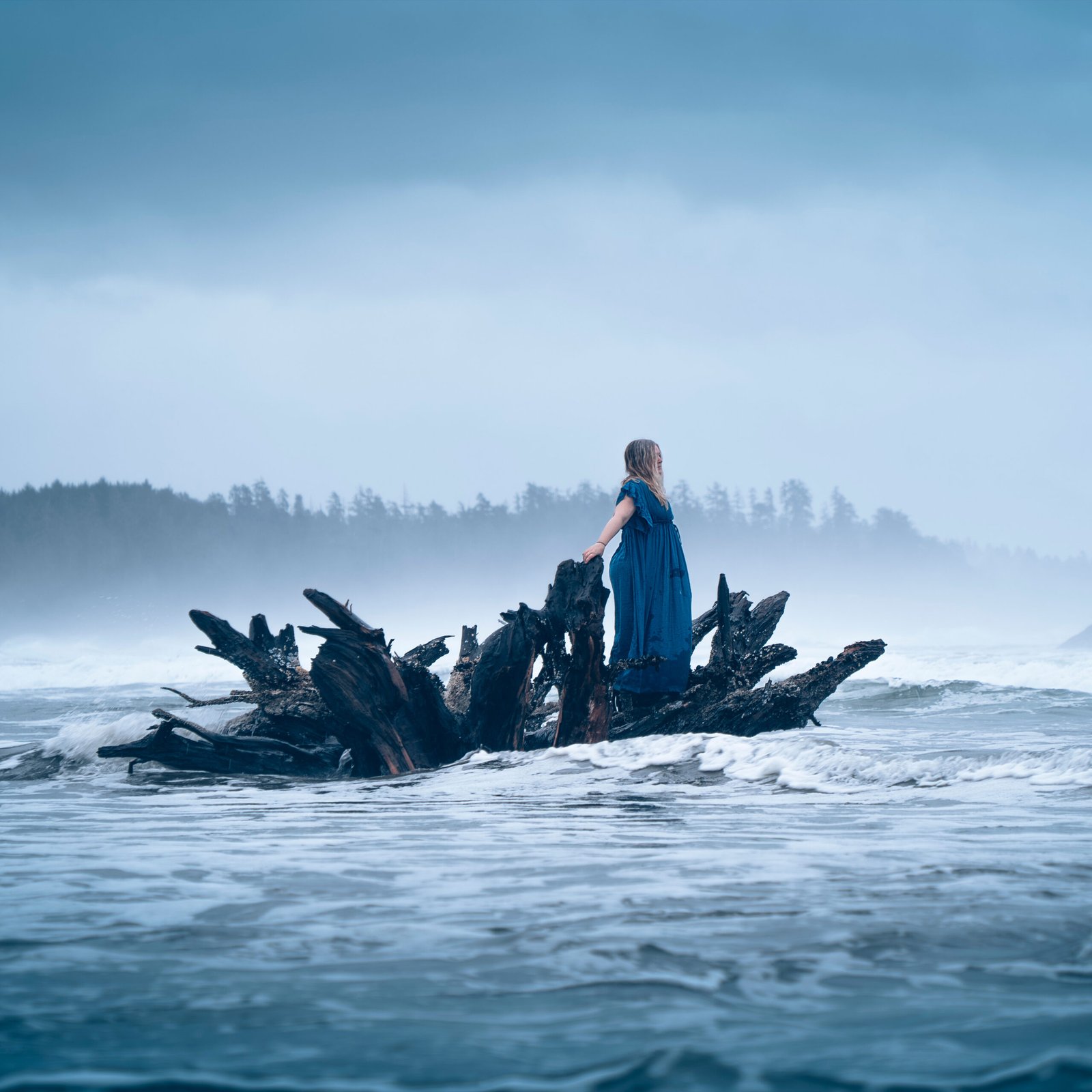 blonde-model-standing-on-log-in-the-ocean-looking-the-horizon-taking--a-professional-photoshoot-in-Tofino