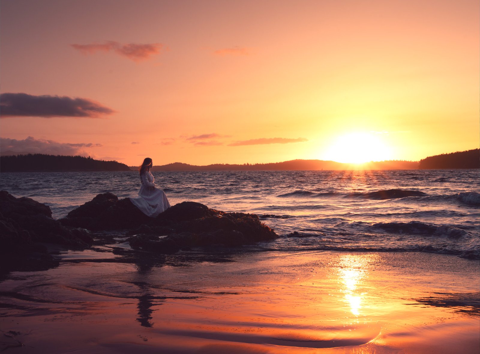 professional portrait at sunset golden hours photoshoot beautiful woman seating on the rocks by the ocean looking the horizon in Vancouver Island